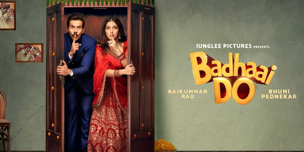 Homem e mulher indianos, dentro de um armário, fazendo um gesto de silêncio. Fotografias de um casal na parede ao fundo. Capa do filme Badhaai Do.